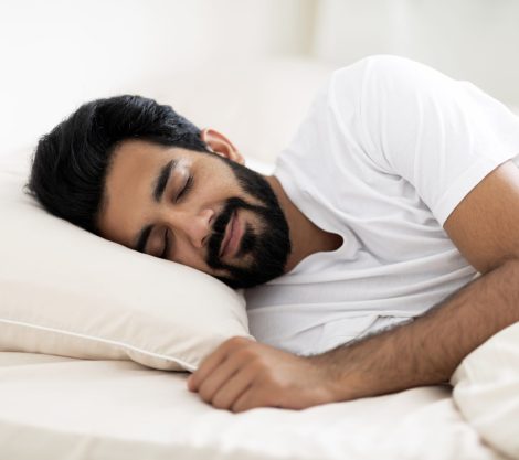 Smiling Young Indian Man Sleeping Calmly In Comfortable Bed At Home, Closeup Shot Of Relaxed Handsome Eastern Male Napping In Cozy Bedroom, Millennial Guy Lying On Soft Pillow With Hand Under Head